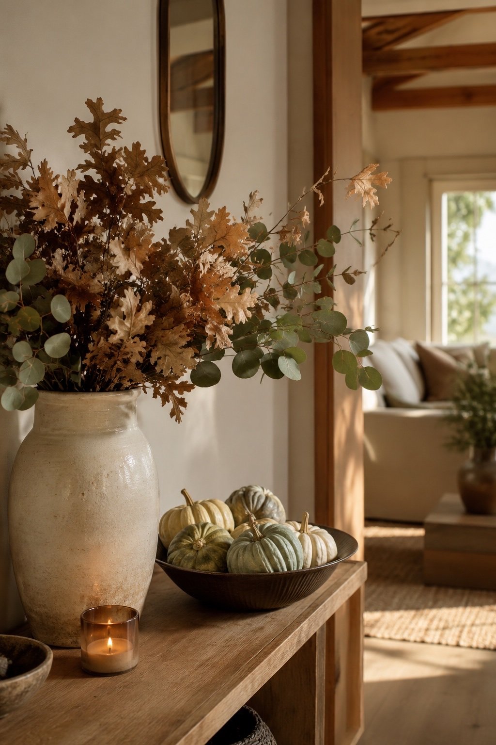 Dried oak branches in a tall vase with muted heirloom pumpkins on a wooden console