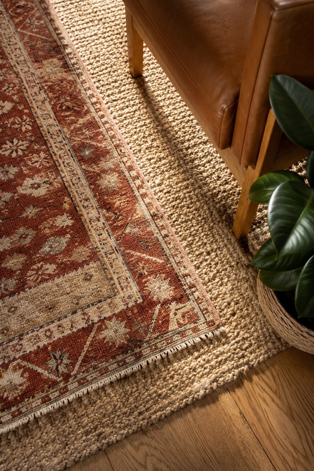 Layered rugs: a small rust and cream wool rug over a large natural jute base